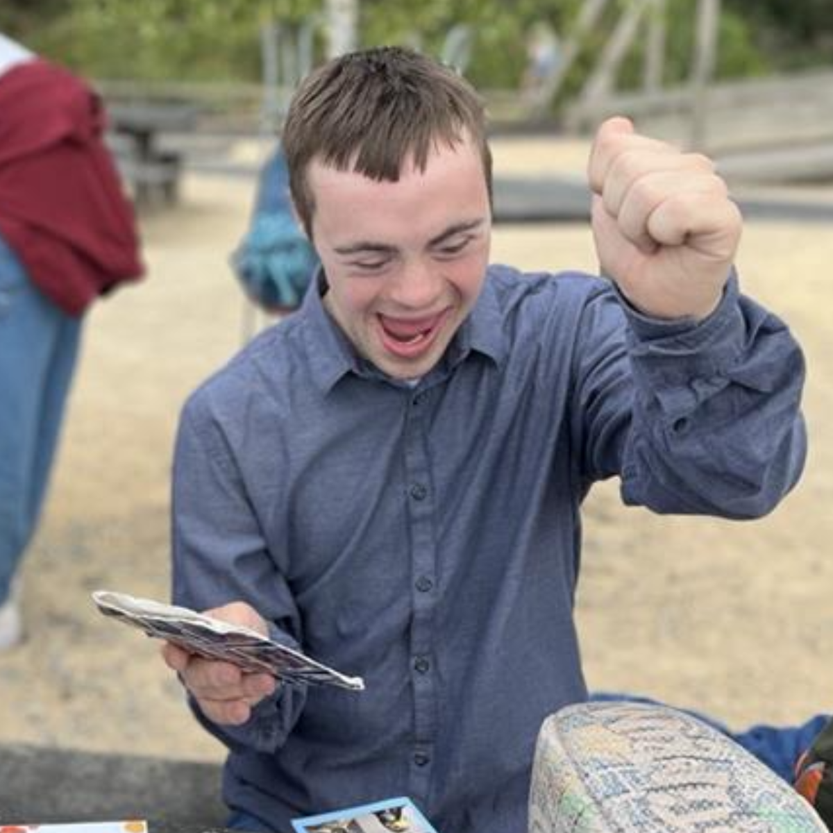 A young man with Down syndrome smiles broadly, holding cards and raising a fist in excitement.