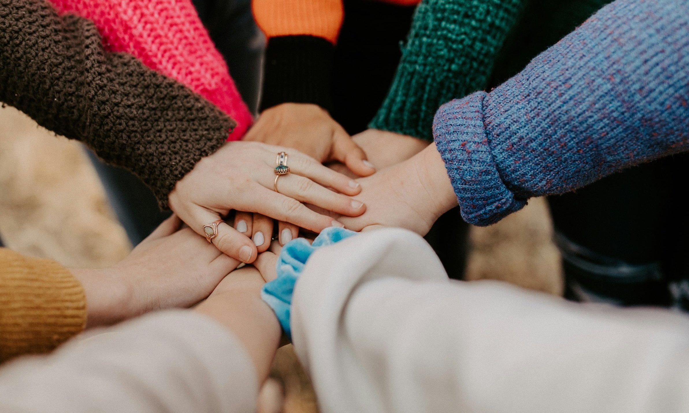 A close-up shot of several hands with rings stacked on top of each other, wearing colorful sweaters, showing unity and togetherness.