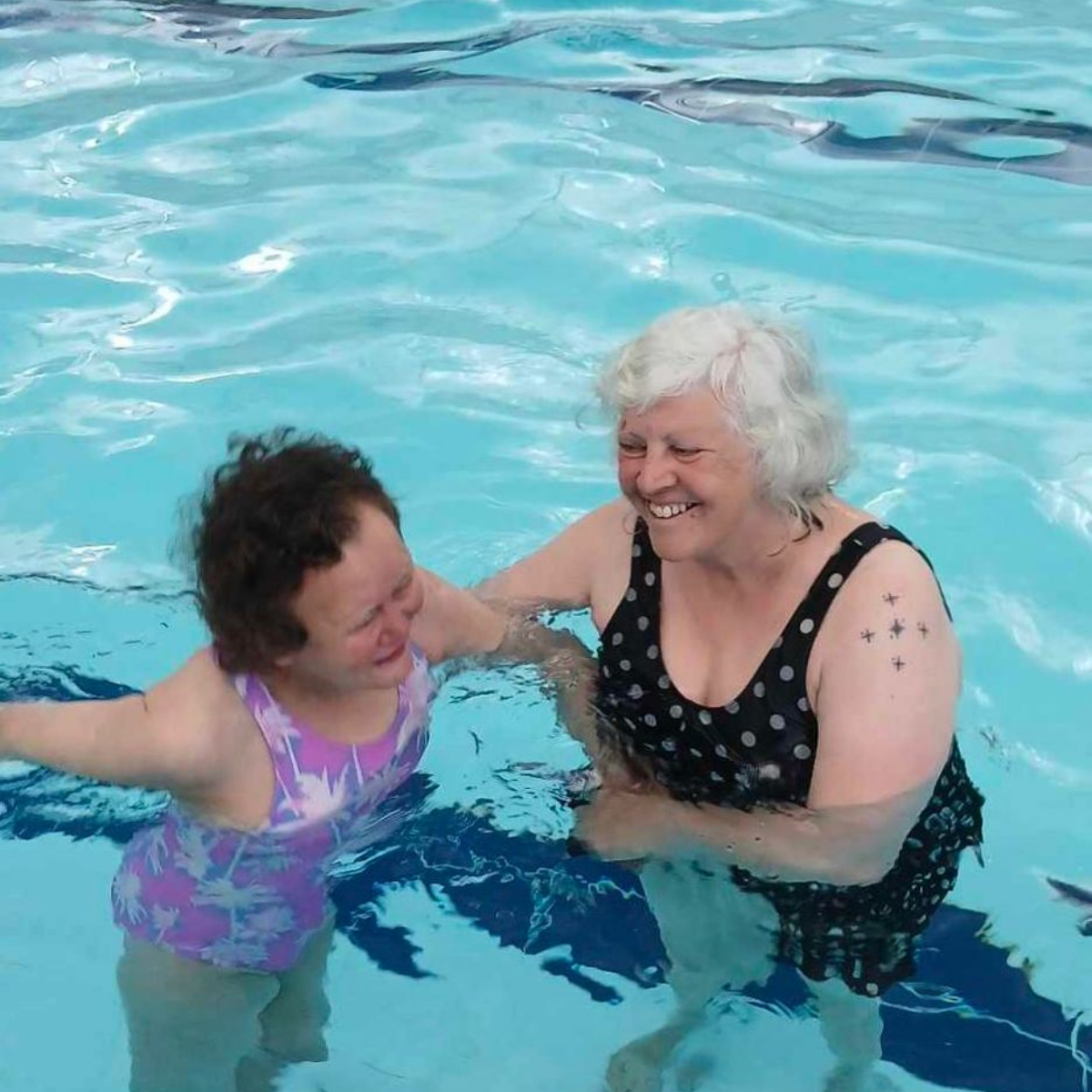 Two women smile while enjoying a swim in a pool.