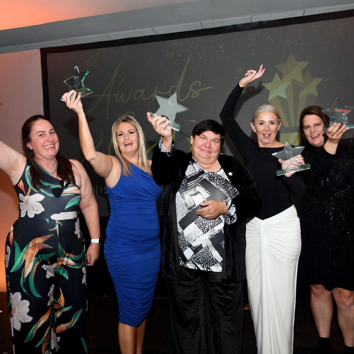 Five women celebrate winning awards, holding up star-shaped trophies.